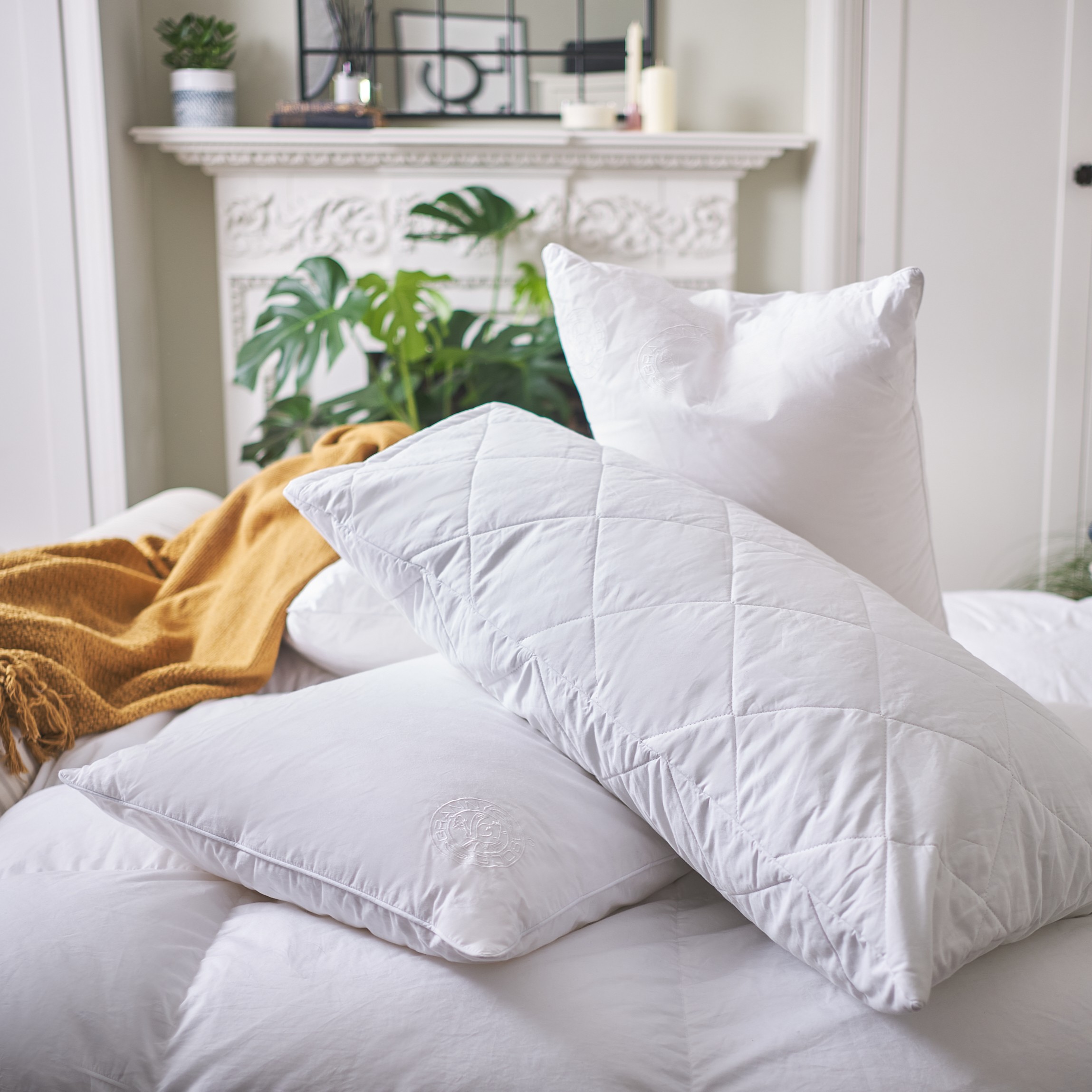 A pile of down alternative pillows on a bed with a mustard knitted throw