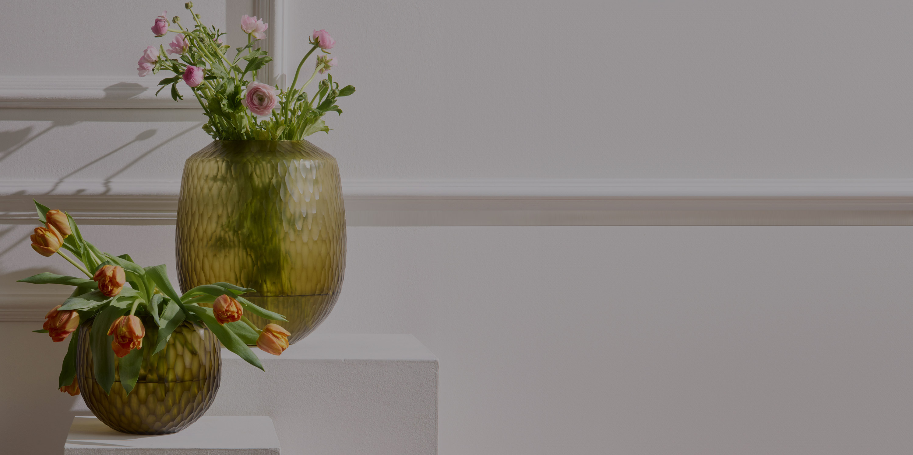 Two green glass vases on a table with flowers