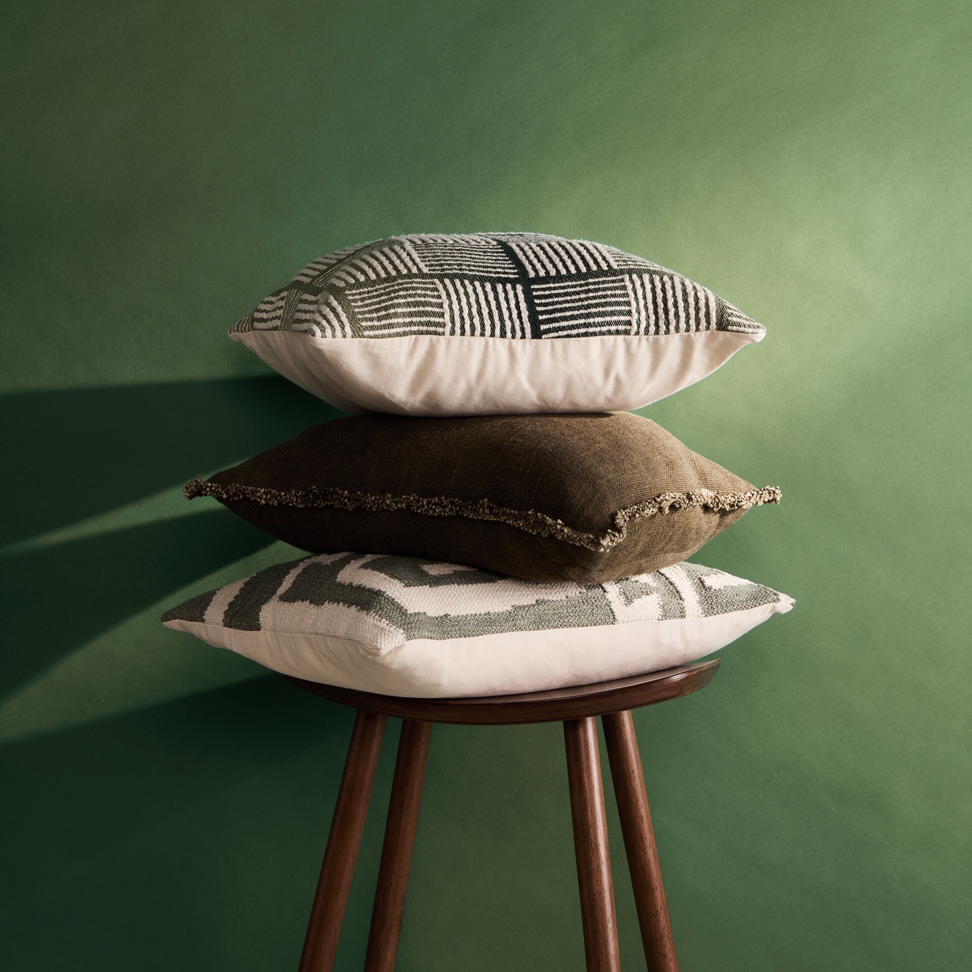 A pile of three patterned cushions in front of a green wall