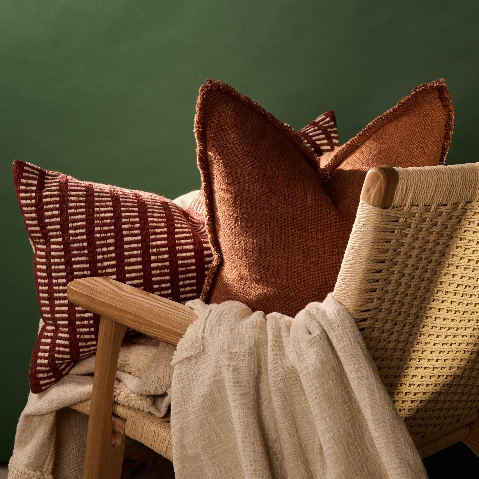 Two rust coloured cushions and a cream throw on a wooden armchair