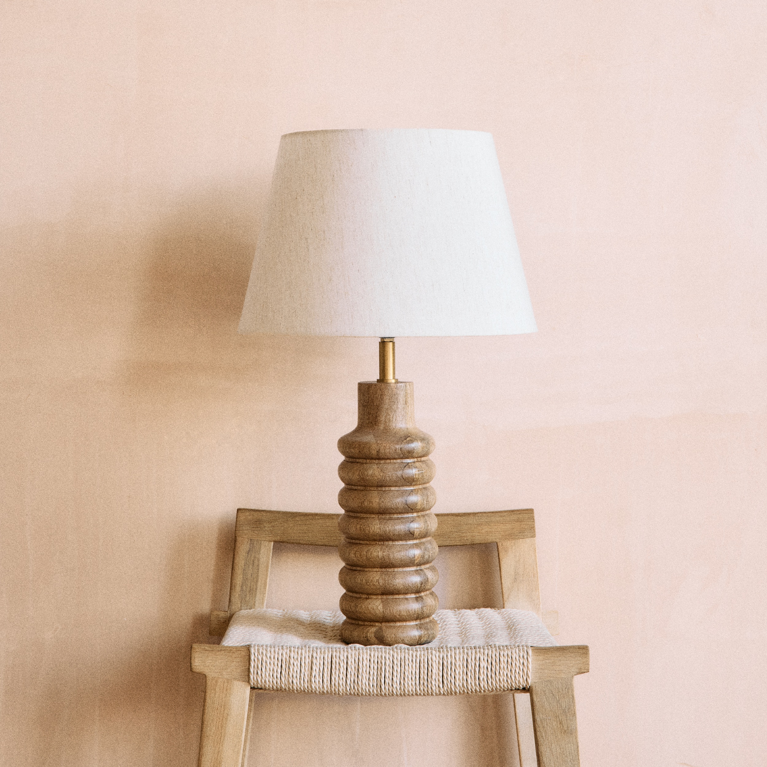 A wooden sculpted lamp with a white lampshade on a wooden chair