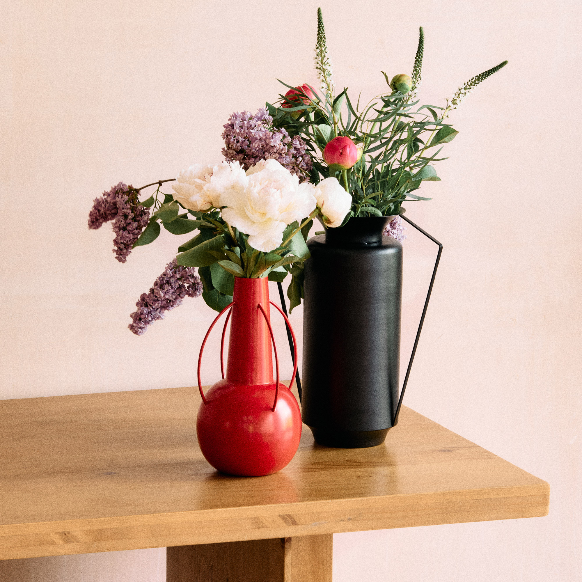 Two metal vases with flowers on a wooden table