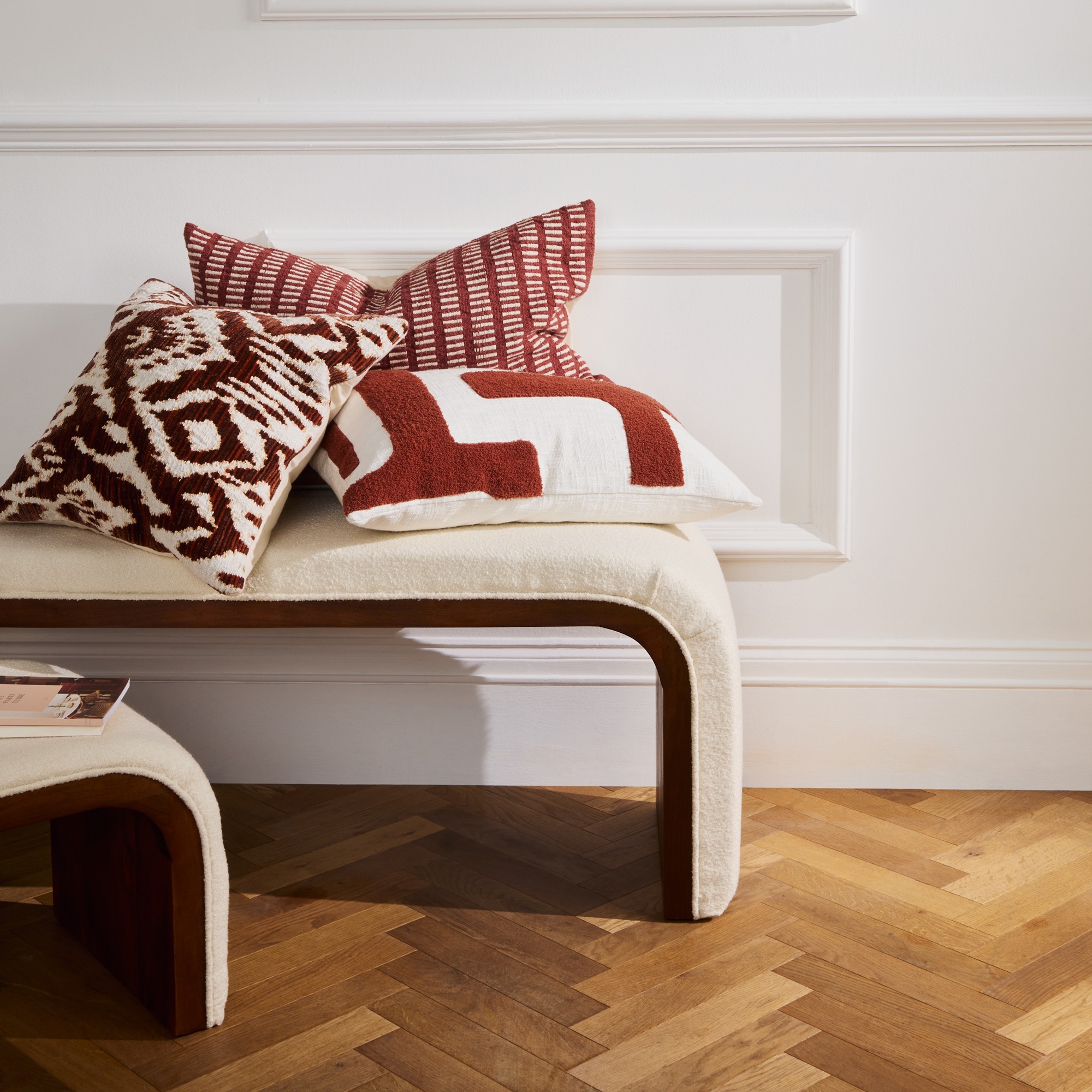 A pile of red and cream cushions on a white upholstered bench
