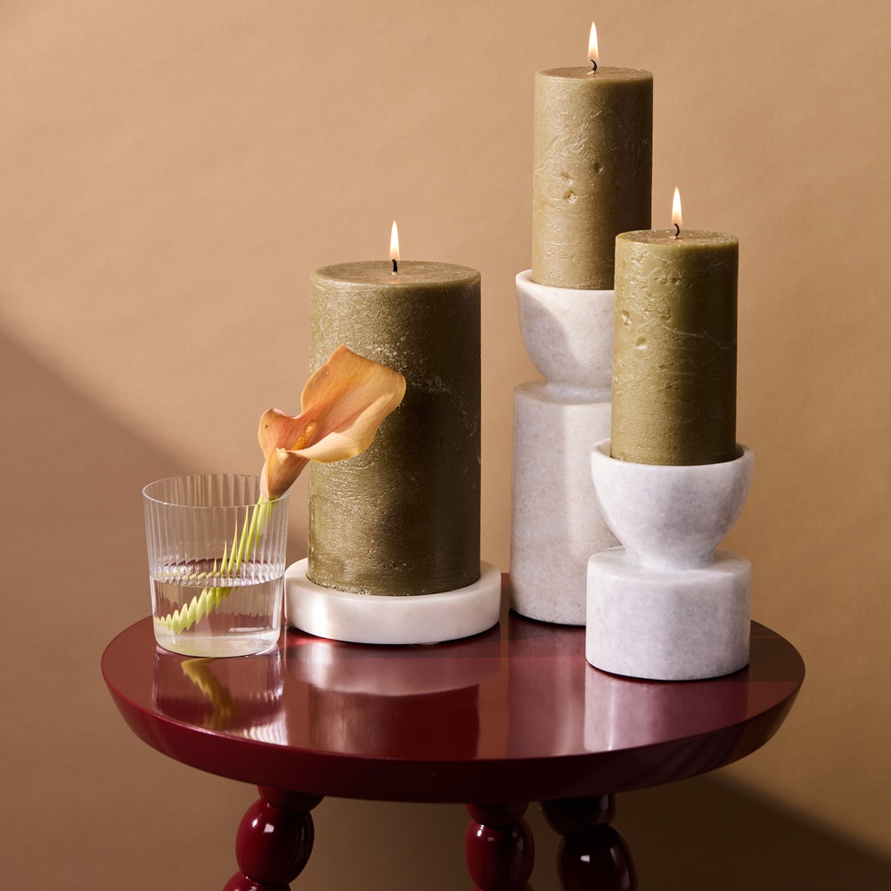 Green pillar candles and marble candle holders on a lacquered wooden table