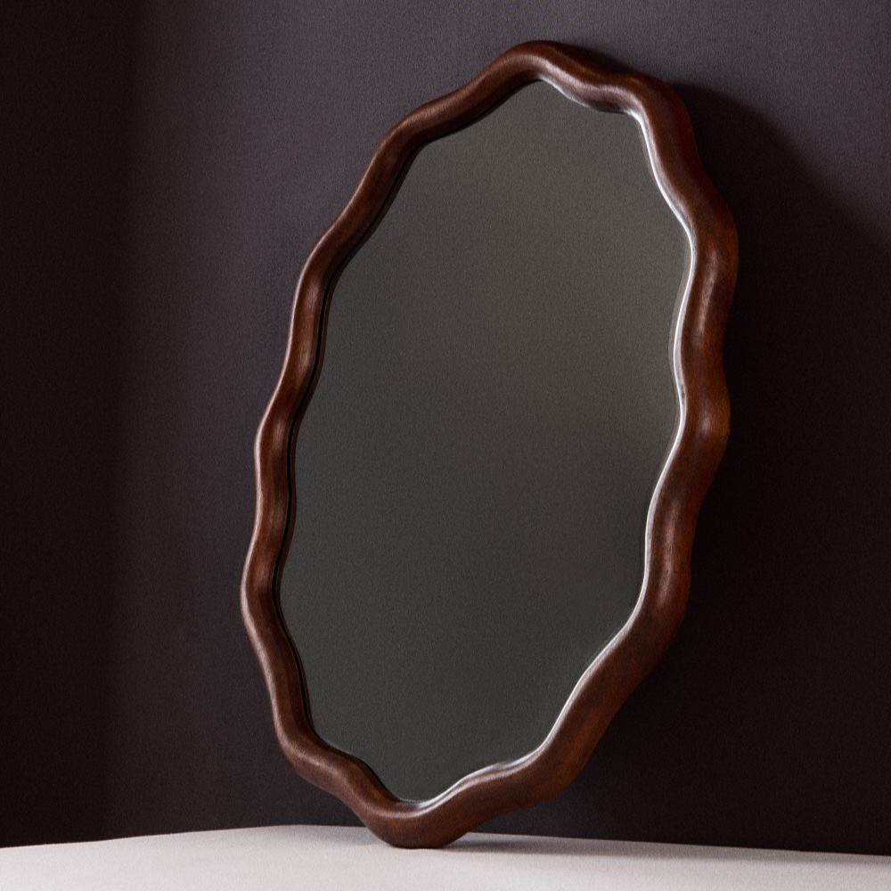 Tall red bobbin mirror against a wall in a hallway next to wood sculpted candle holders